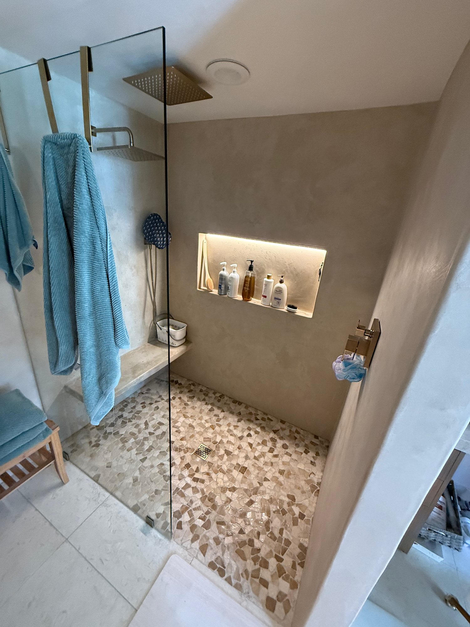 Walk-in shower with a glass panel, pebble floor, built-in bench, and lit niche