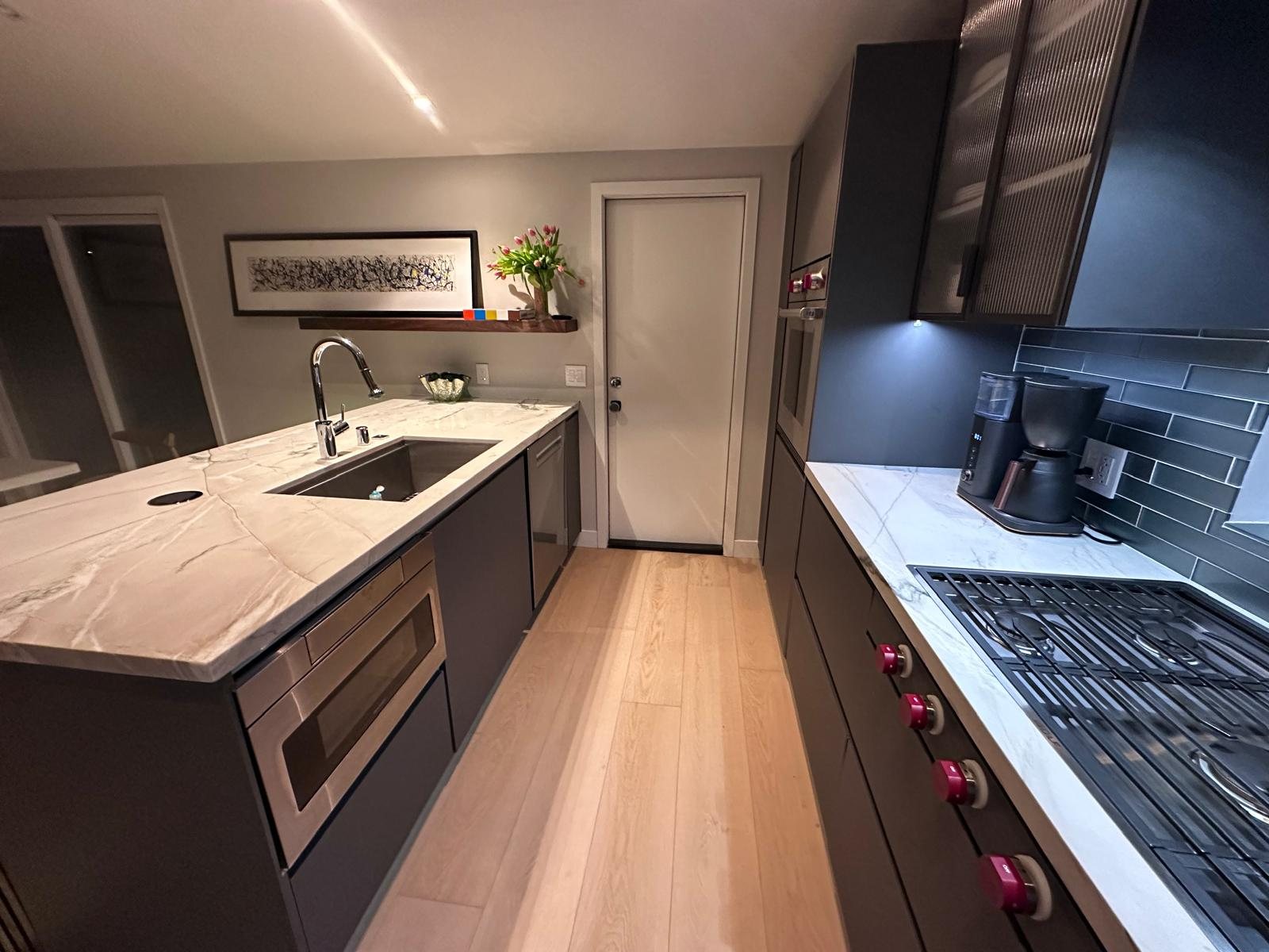 Galley kitchen with dark cabinetry, marble-look counters, undermount sink, and gas range