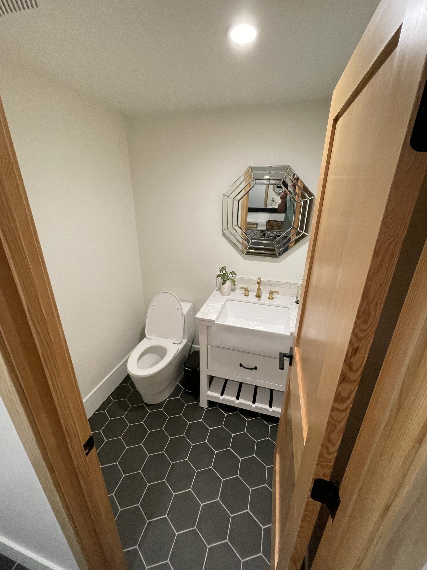 Half bath with hexagon floor tile, a white vanity, and an octagonal mirror