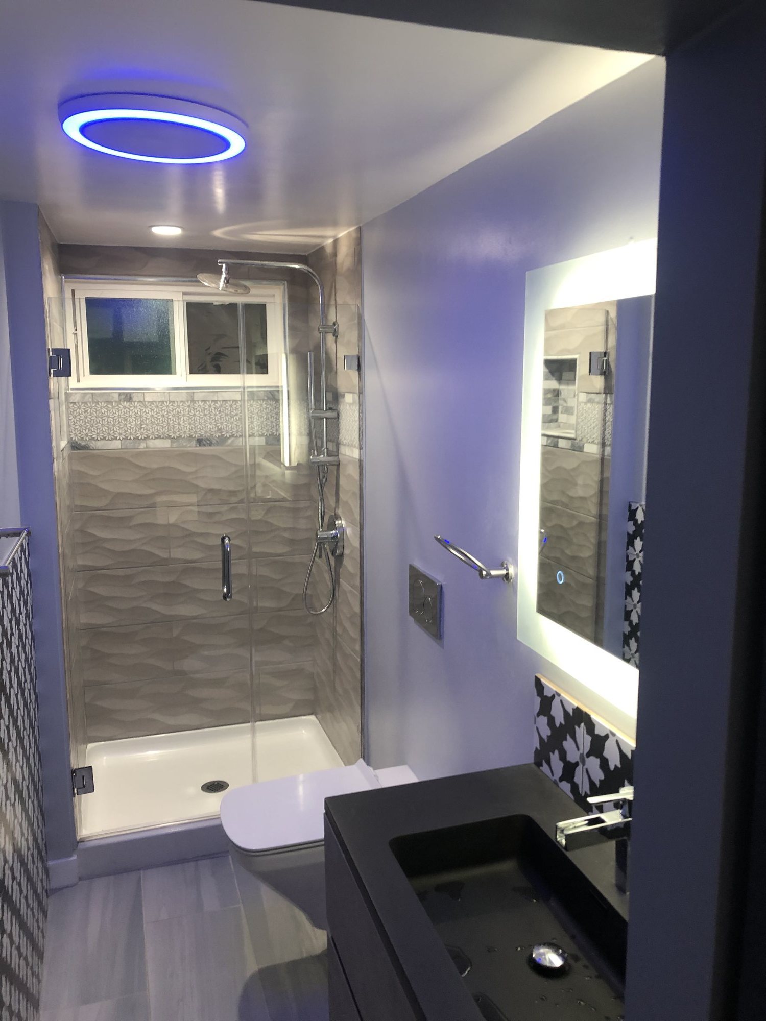 Bathroom with a glass shower, wave-texture tile, black vanity, and backlit mirror