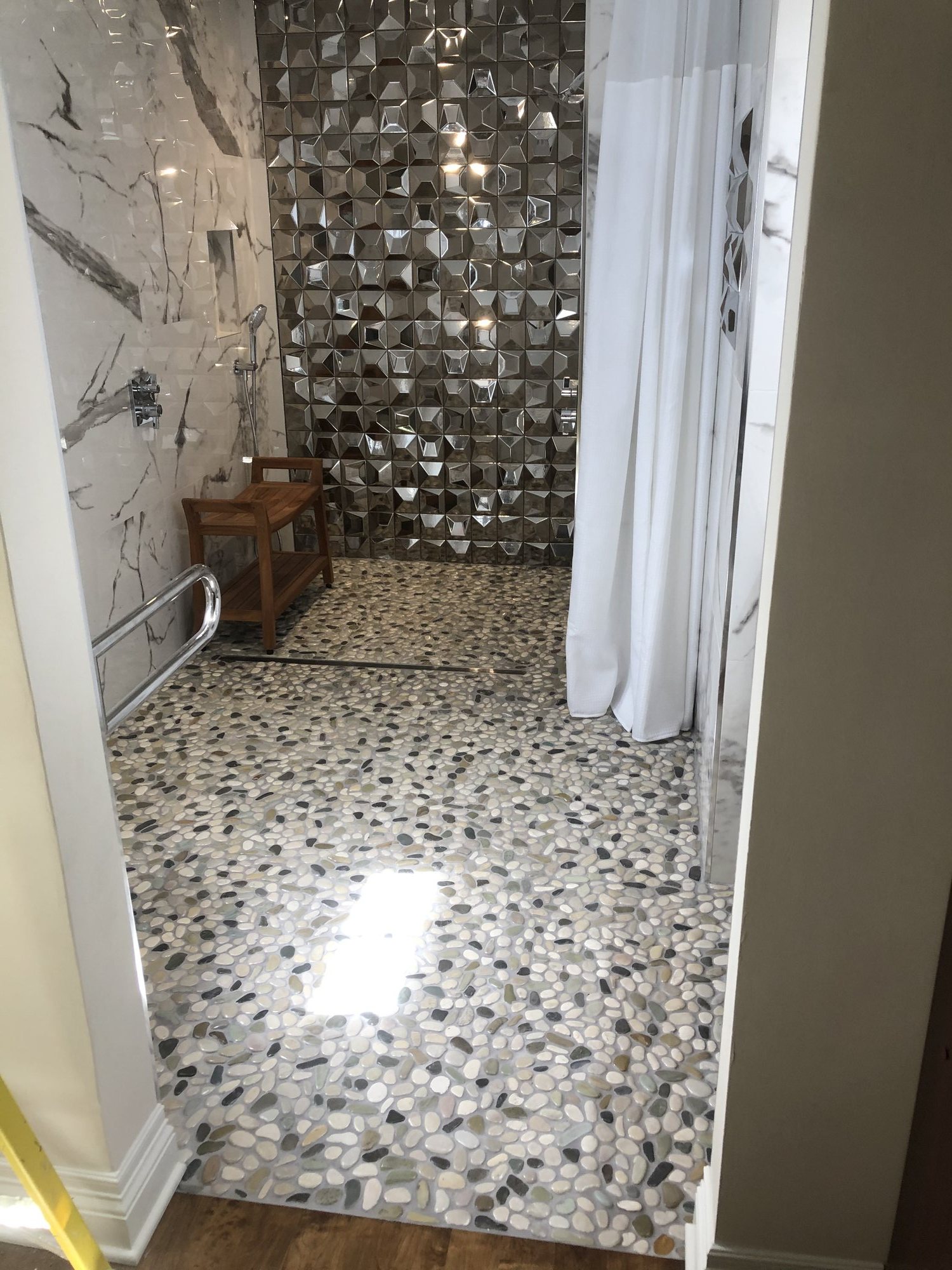 Walk-in shower with a mirrored mosaic accent wall, pebble floor, and grab bar