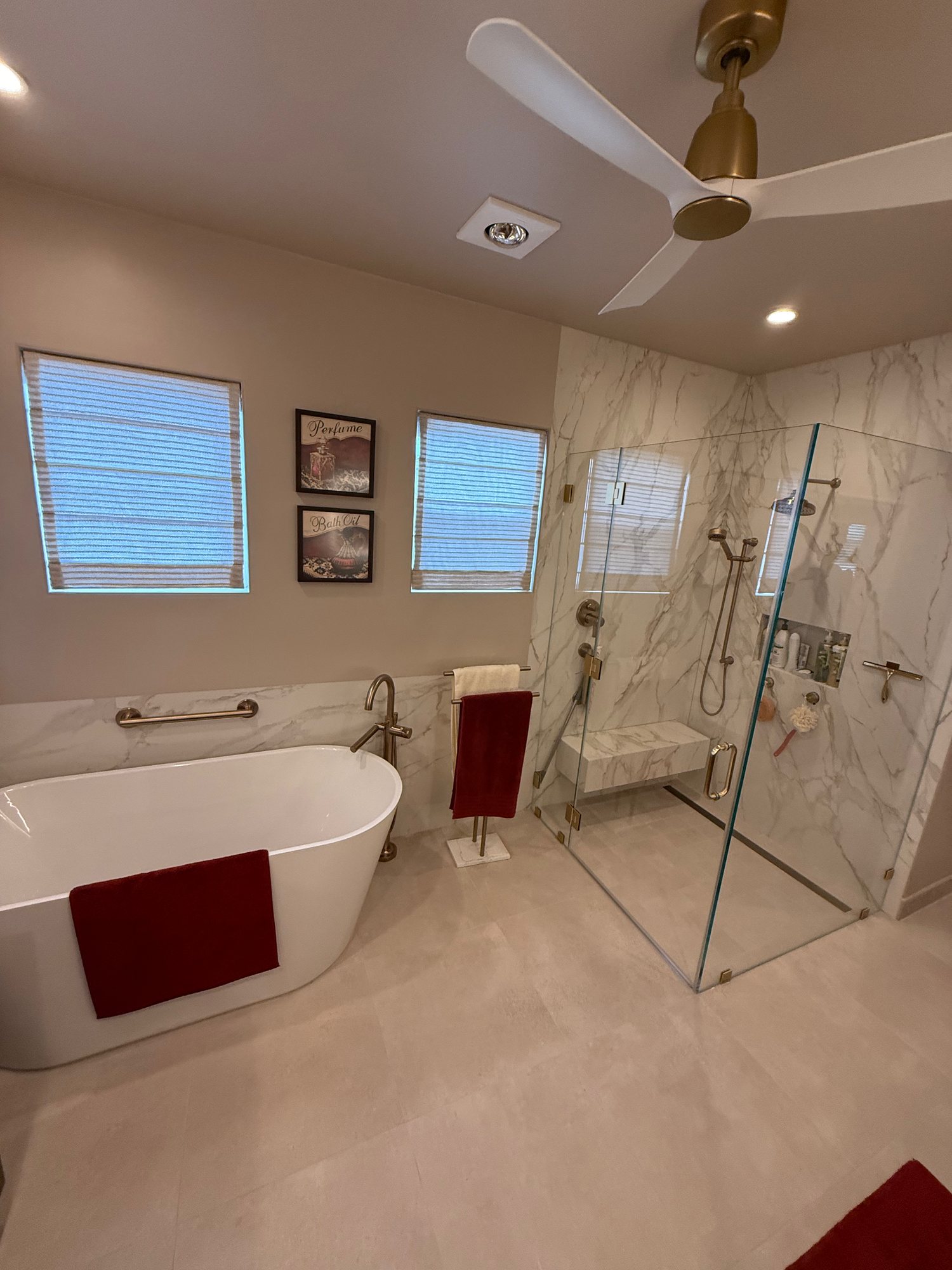 Primary bathroom with a freestanding tub, marble-look glass shower, and ceiling fan
