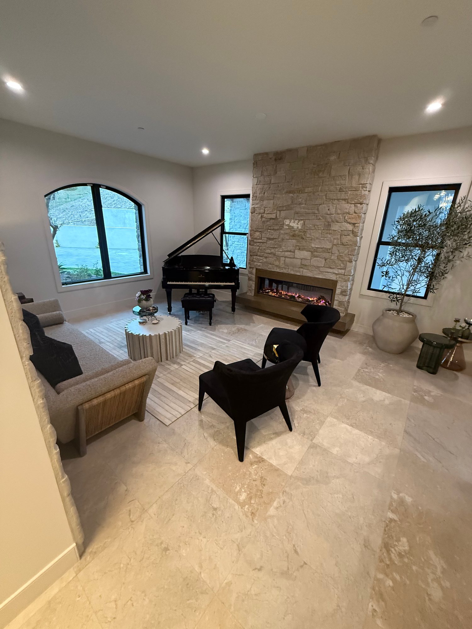 Finished living room with a stacked-stone fireplace wall, arched window, and large-format tile floor