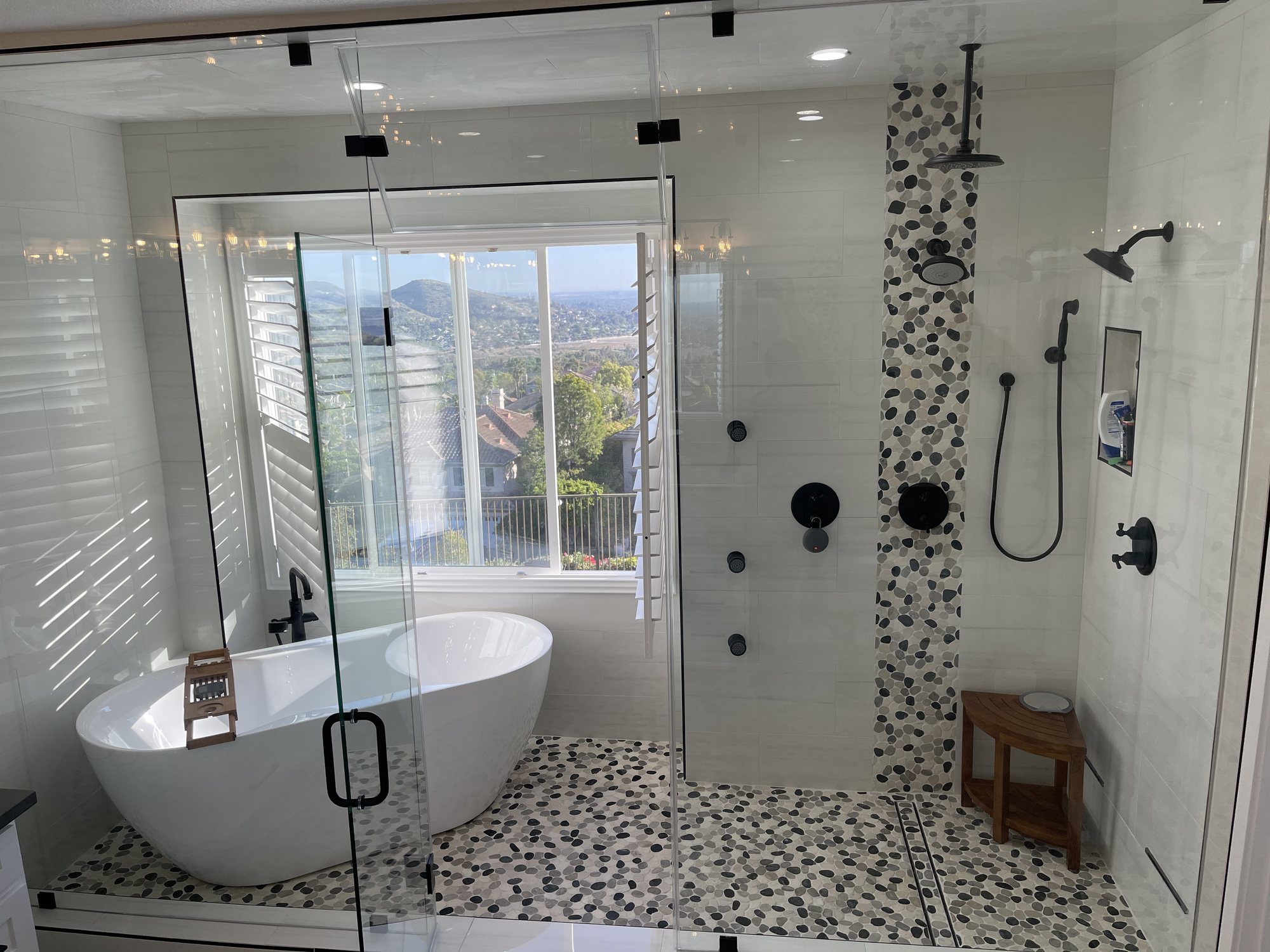 Finished L & E bathroom with a freestanding tub and pebble-tile walk-in shower behind glass, with a hillside view through the window