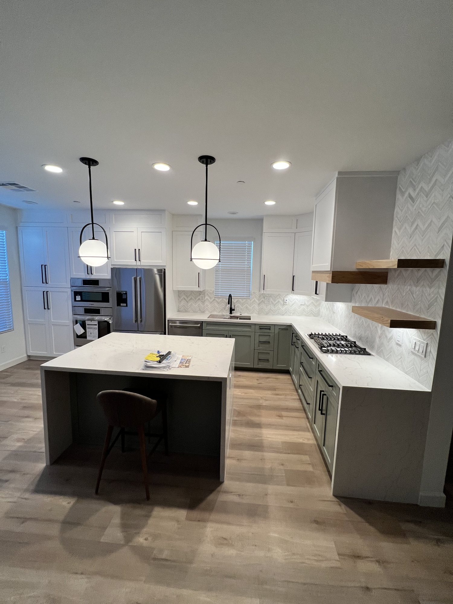 Finished kitchen with white upper cabinets, gray-green lowers, a waterfall island, and globe pendant lights