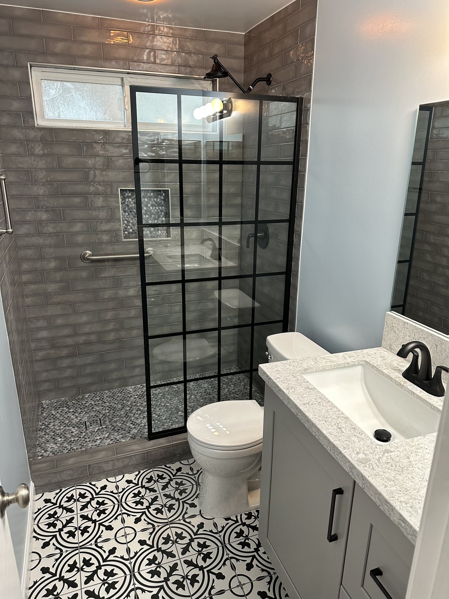 Bathroom with a grid-frame glass shower, gray subway tile, and patterned black-and-white floor tile