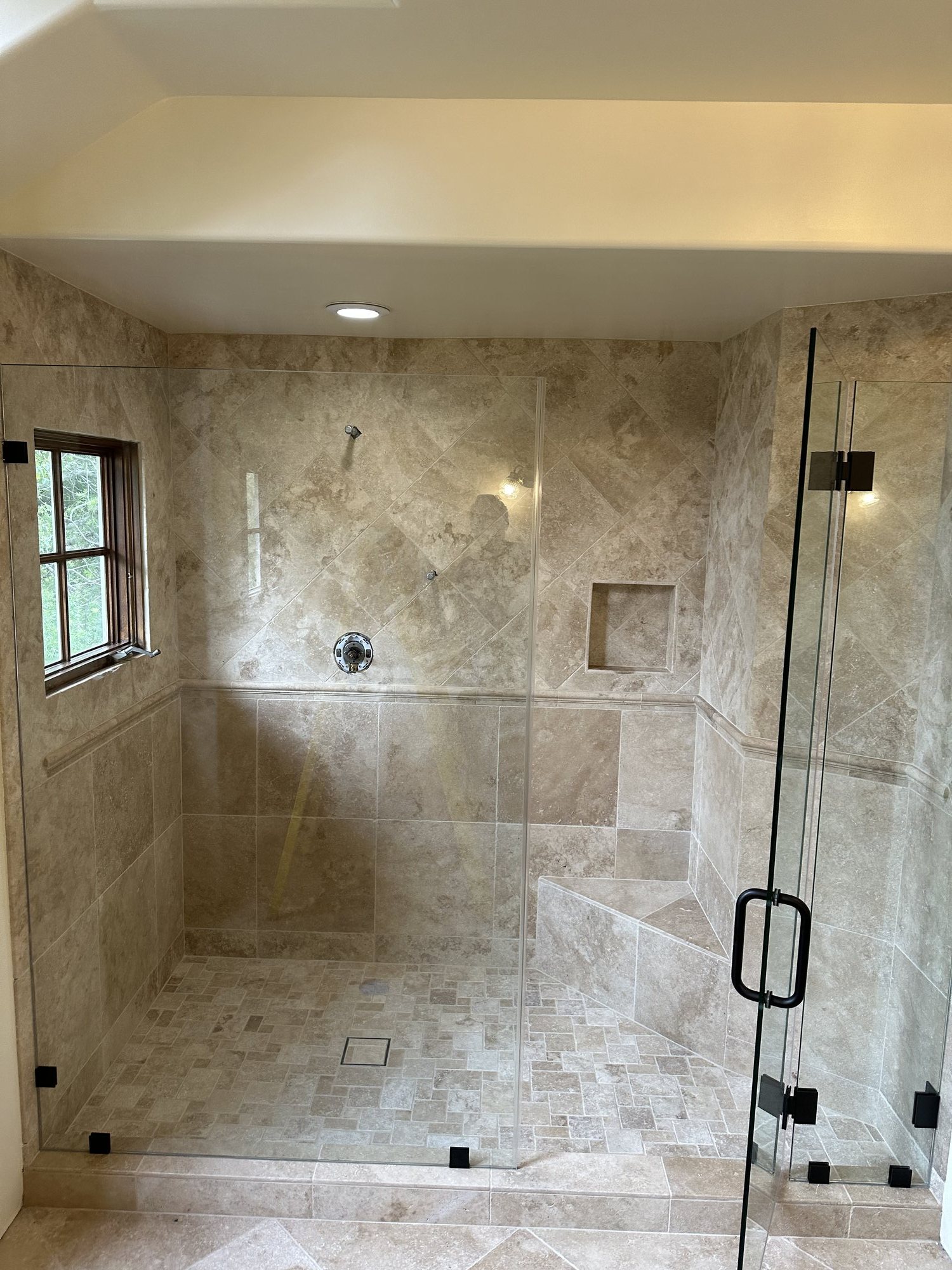 Large tiled walk-in shower with a glass enclosure, corner bench, and recessed niche