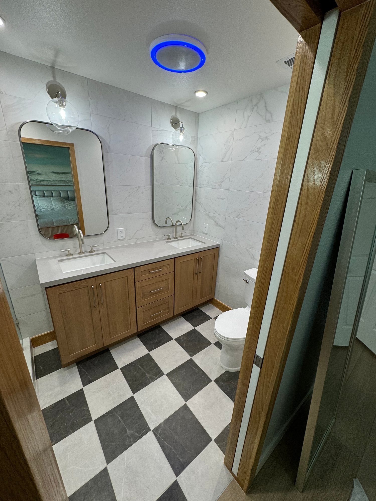 Bathroom with a double wood vanity, rounded mirrors, and a checkerboard tile floor