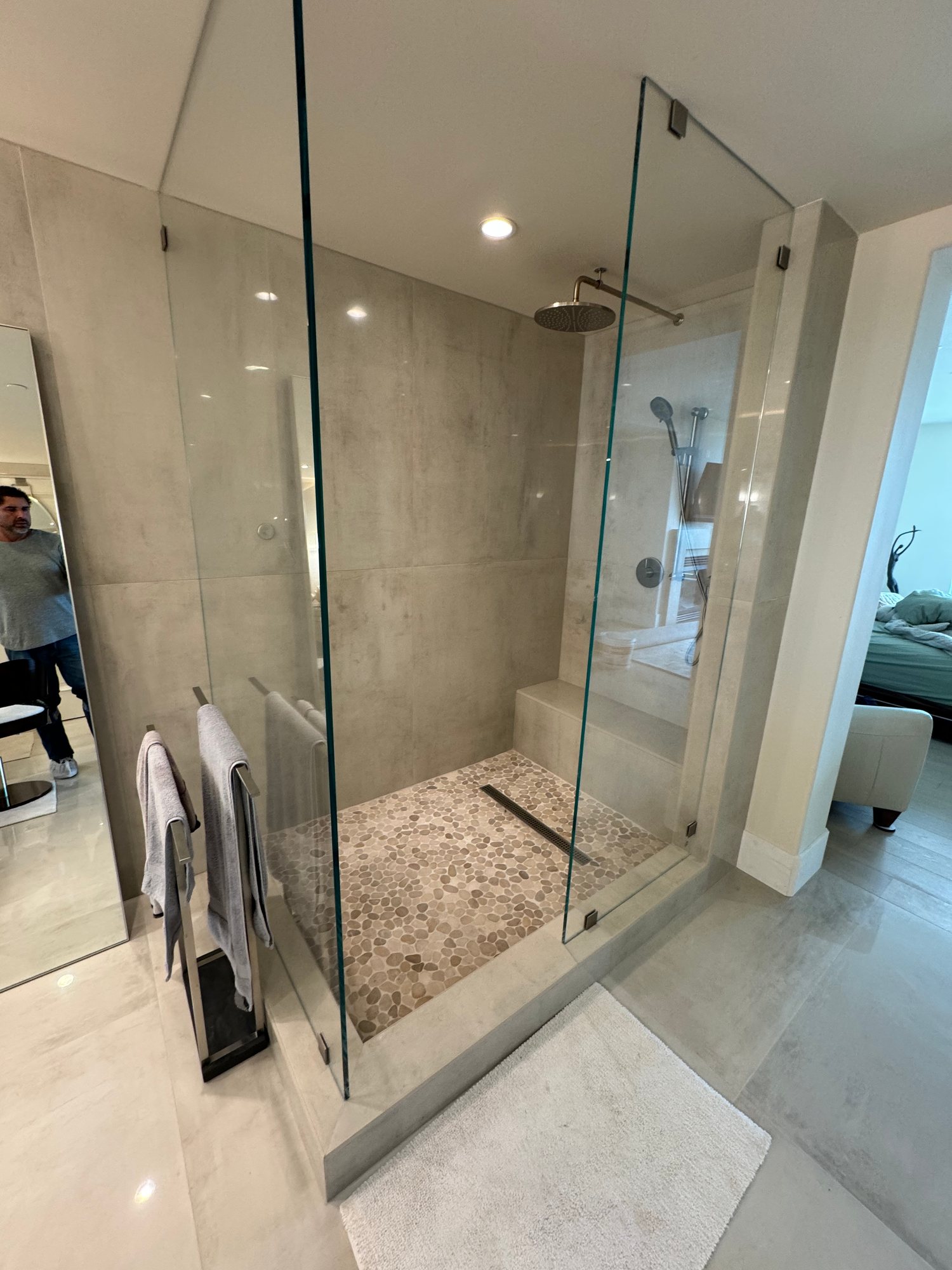 Frameless glass walk-in shower with large-format tile and a pebble floor