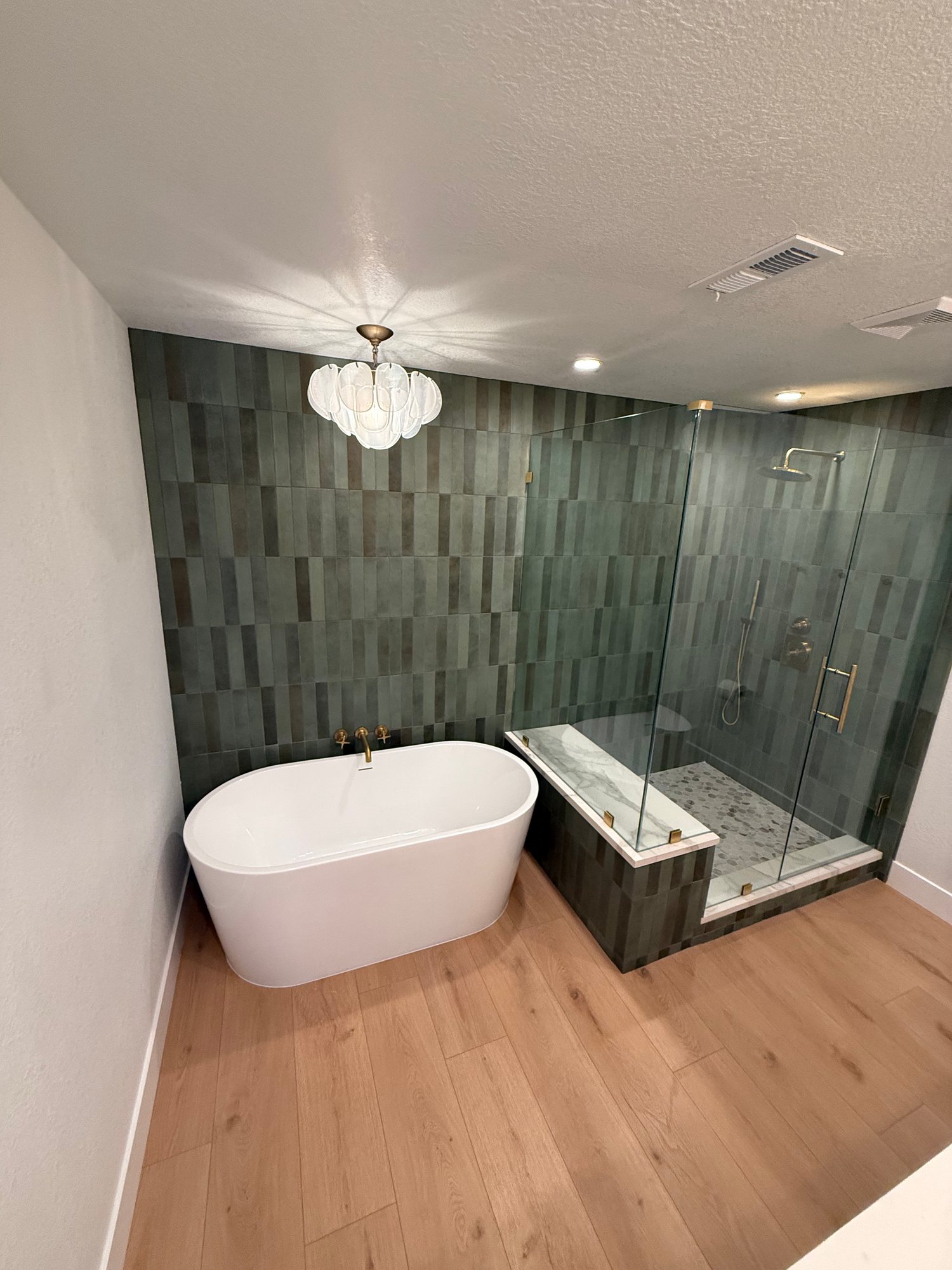 Bathroom with green vertical tile, a freestanding tub, glass shower, and bubble chandelier
