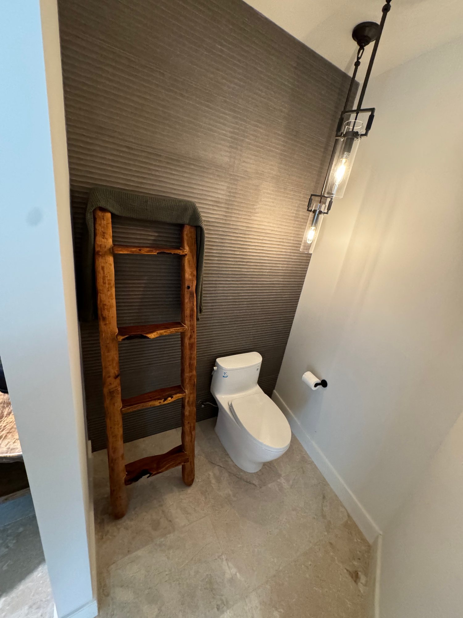 Powder room with a textured dark accent wall, rustic wood towel ladder, and hanging pendant light